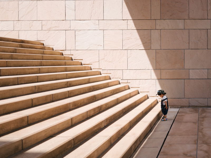 Jeune enfant face à un grand escalier, symbole du chemin vers le dépassement de soi et la sortie de l’éreutophobie
